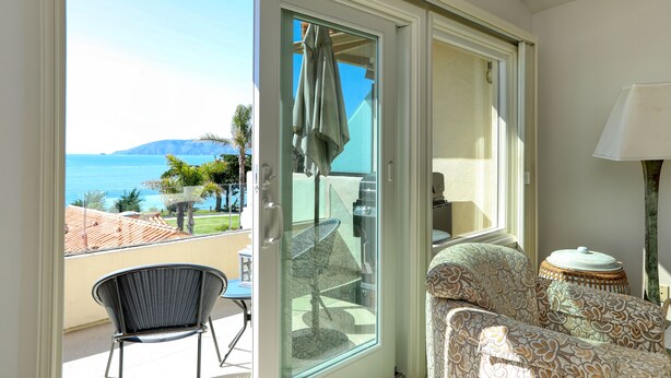 Un balcone con vista sul mare, una sedia in vimini, un divano a fantasia e una lampada.