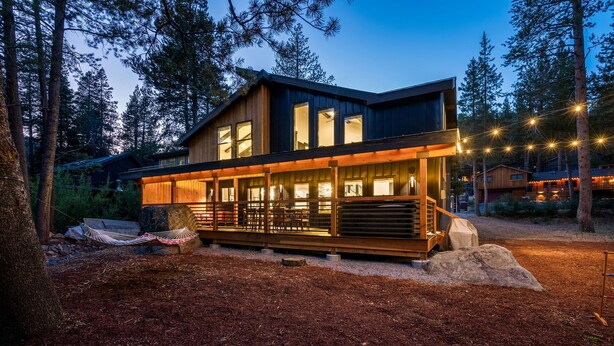 A modern two-story cabin with large windows, a wooden deck, and a stone fireplace. - Pet-Friendly Tahoe Escape | Hot Tub | King Suite | Arcade | Near Trails & Lake (Olympic Valley)