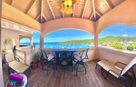 A covered outdoor area with a table and chairs, a view of the sea, and potted plants.