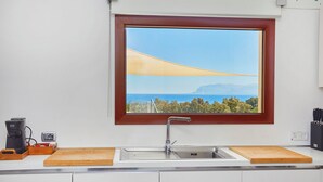 Een keuken met een raam, een spoelbak, een snijplank en een koffiezetapparaat.