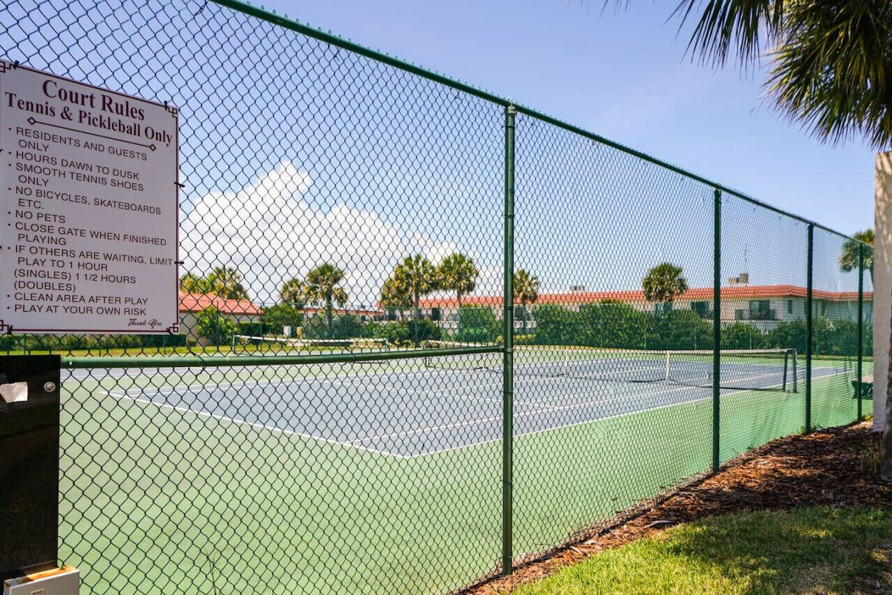 Un terrain de tennis entouré d’une clôture en treillis métallique et sur lequel est affiché un panneau indiquant les règles à respecter.