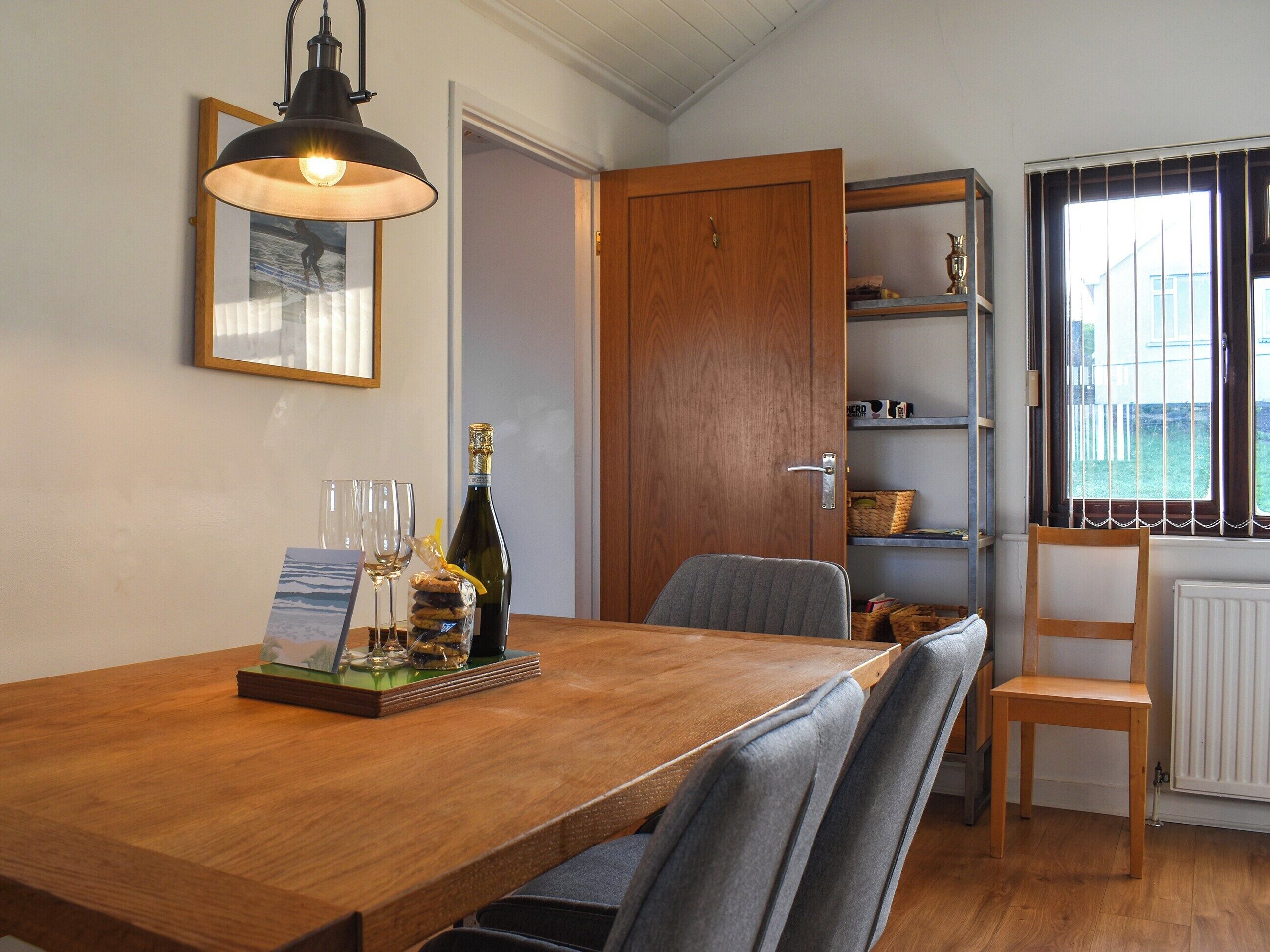 A dining area with a wooden table, two chairs, a bottle of champagne, and a framed picture on the wall.