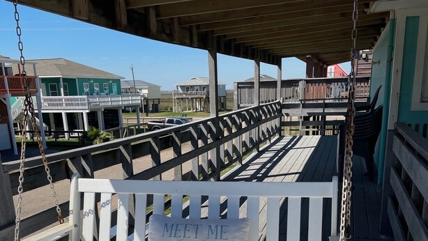 A wooden deck with a white swing bench featuring a pillow with "MEET ME BY THE SEA" text. - Family fun! Perfect for families to make memories (Freeport)