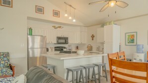 A modern kitchen with white cabinets, a central island with stools, a refrigerator, and a microwave. - Family fun! Perfect for families to make memories (Freeport)