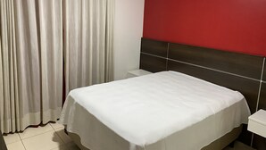 A hotel room with a bed, a nightstand, a red accent wall, and a window with curtains. - Sobrado Tranquilo, rua Silenciosa (Jardim São Paulo São Paulo)