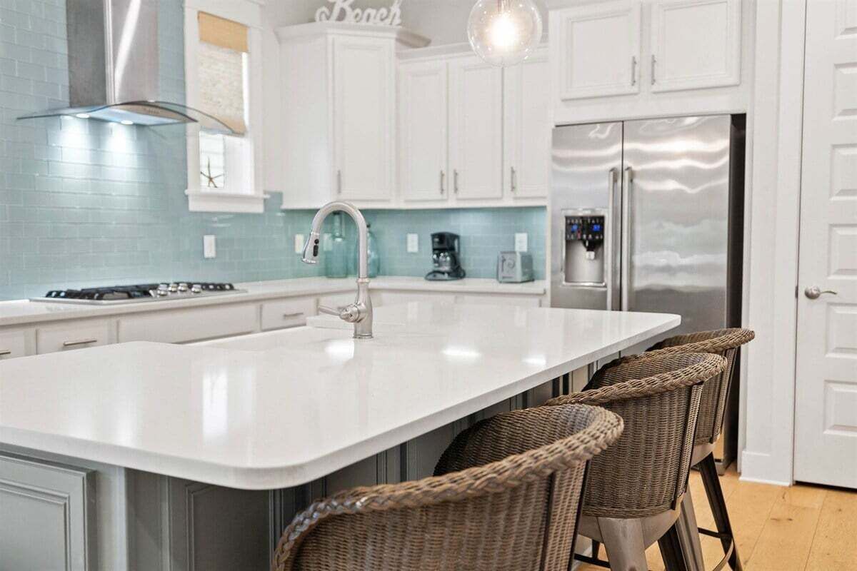 A fresh and modern kitchen with white cabinetry, turquoise backsplash, and high-end finishes.