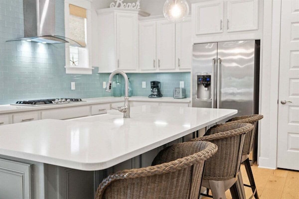 A fresh and modern kitchen with white cabinetry, turquoise backsplash, and high-end finishes.