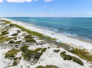 A beach with a wooden boardwalk leading to a structure with a glass roof.