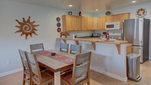 A compact kitchen with wooden cabinets, a microwave, a stainless steel refrigerator, and a dining area with a table and chairs. - The Howling Coyote - Moab's Adventure Basecamp (Moab)