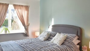 A bedroom with a bed, a bedside table, a lamp, and a window with curtains. - 2 bedroom accommodation in Mundesley (Mundesley)