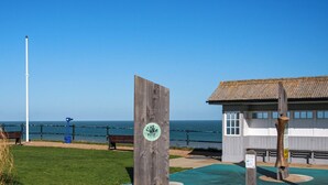 A coastal area with a wooden structure, a bench, and a signboard. - 2 bedroom accommodation in Mundesley (Mundesley)