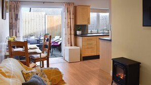 A cozy living room with a sofa, a dining area with a table and chairs, a kitchen with wooden cabinets, and a black wood-burning stove. - 2 bedroom accommodation in Mundesley (Mundesley)
