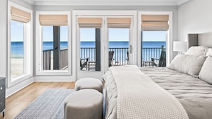Une chambre avec un grand lit, une vue sur la plage et un balcon aménagé avec du mobilier d’extérieur.