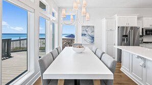 Une cuisine moderne avec des meubles blancs, un réfrigérateur en acier inoxydable et un coin repas comprenant une table blanche et des chaises grises.