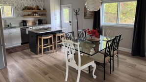Uma cozinha moderna com armários brancos, uma ilha central e uma área de refeições com mesa de vidro e cadeiras brancas.