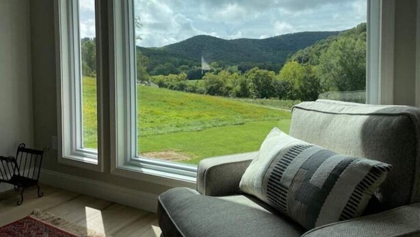 Quarto com uma janela ampla que oferece vista para um campo verde e colinas.