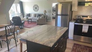 Cozinha moderna com ilha central, eletrodomésticos de aço inoxidável e área de jantar com cadeira e mesa.