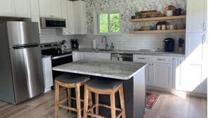 Uma cozinha moderna com armários brancos, uma geladeira de aço inoxidável, micro-ondas e uma ilha grande com banquetas.
