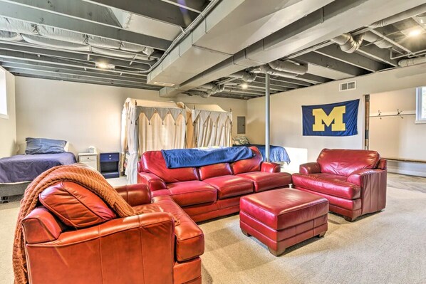 A room with a red leather sectional sofa, a red leather armchair, and a matching ottoman. A large 'M' flag is visible on the wall.