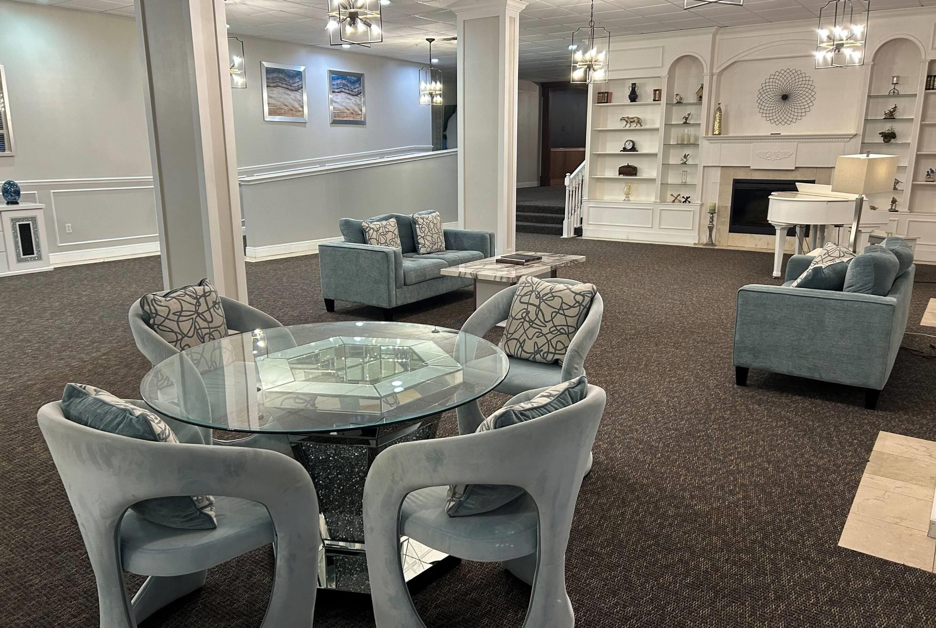 A modern lounge area with a glass-top table surrounded by chairs, a fireplace, and a staircase leading to another level.