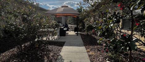 A pathway leading to a gazebo with a view of a garden and a building in the background.