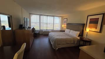 A hotel room with a bed, a desk, a chair, a TV, and a window with blinds.