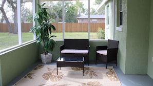 A covered patio area with two wicker chairs, a small table, and a potted plant.