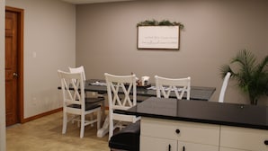 A dining area with a table and four white chairs, a black countertop, and a wall-mounted sign.