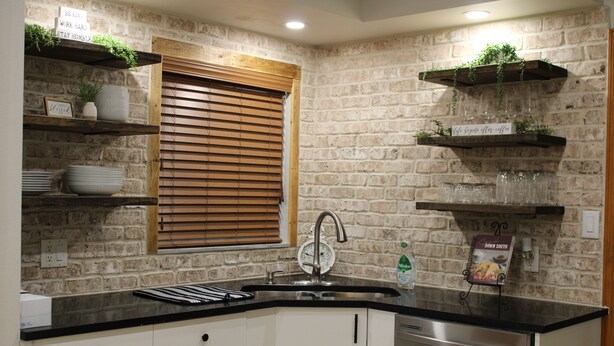 A kitchen with a brick wall, wooden shelves, a sink, and a dishwasher.