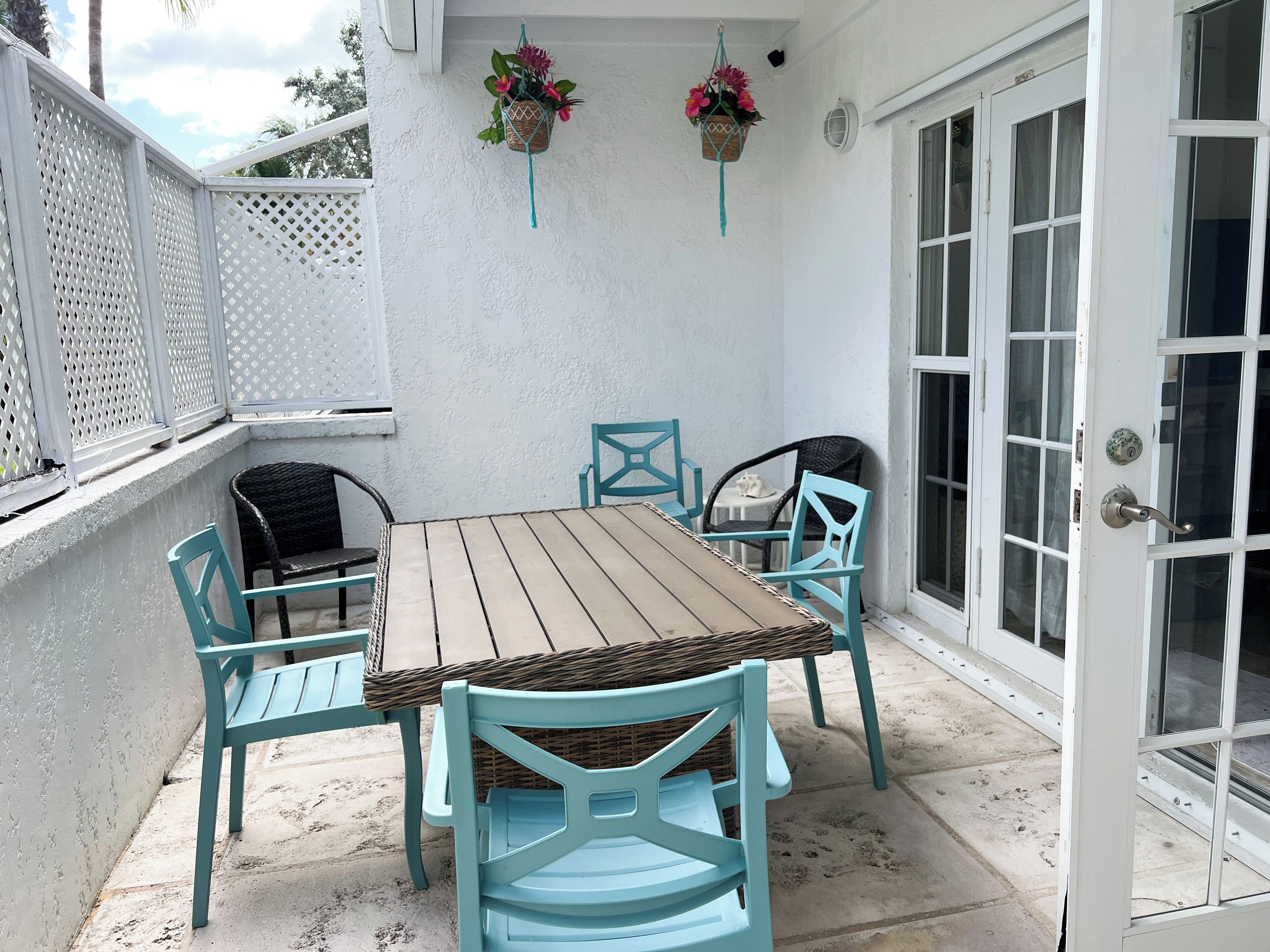 Un patio con una mesa de madera y cuatro sillas, una pared blanca y una puerta con paneles de vidrio.