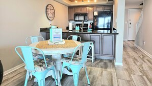 A dining area with a round table and four chairs, a kitchen with modern appliances, and a clock on the wall. - Pensacola Beach Waterfront Condo with Relaxing View. Family Friendly! (Pensacola Beach)