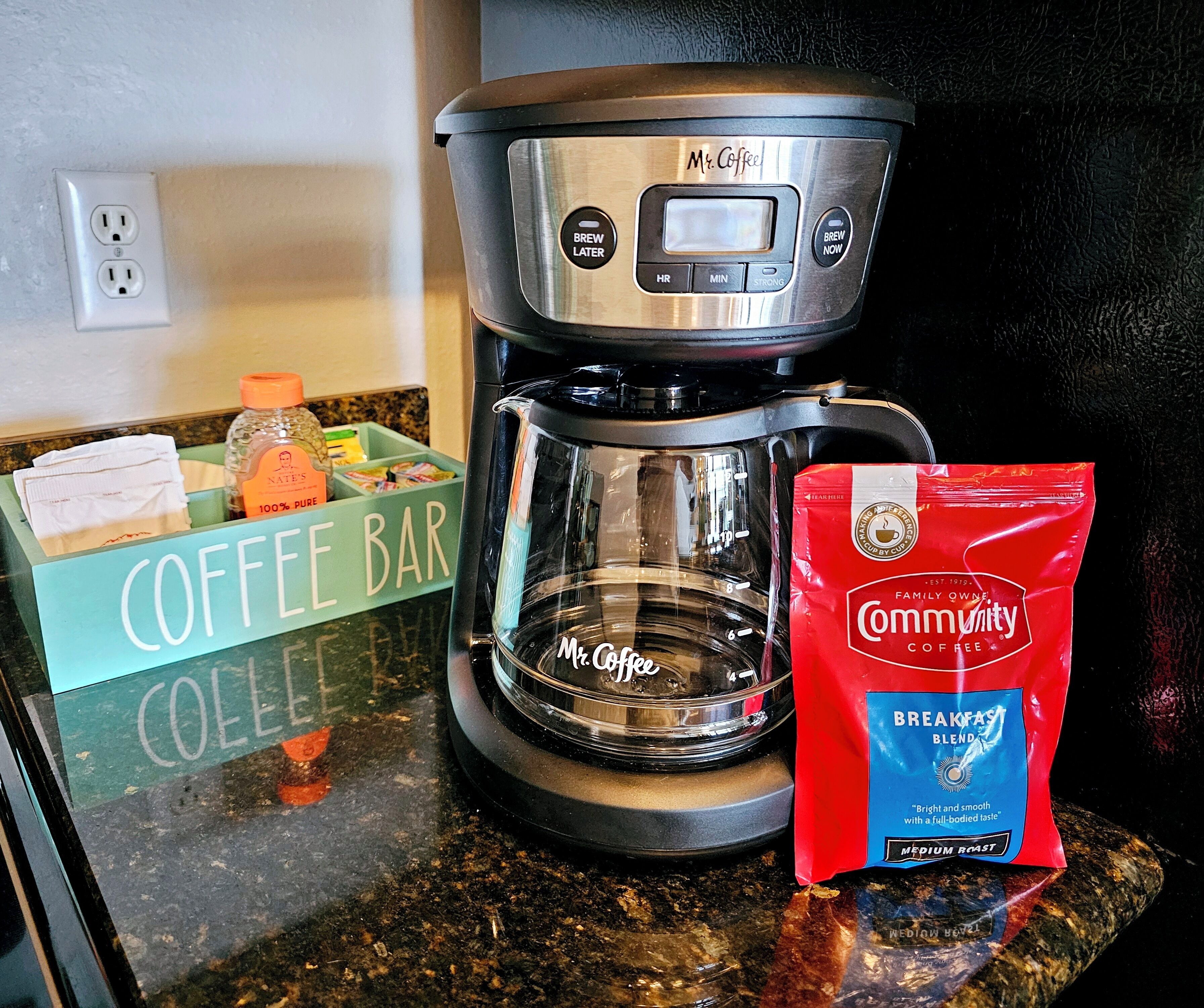 Eine Kaffeemaschine, ein Kaffeeautomaten und eine Packung Community Coffee stehen auf einer Küchenarbeitsplatte.