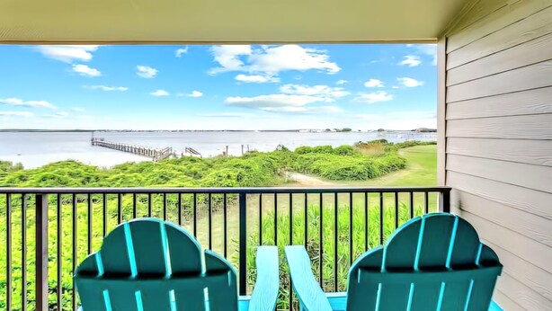 A balcony with two chairs, a view of a body of water, and a bridge in the distance. - Pensacola Beach Waterfront Condo with Relaxing View. Family Friendly! (Pensacola Beach)
