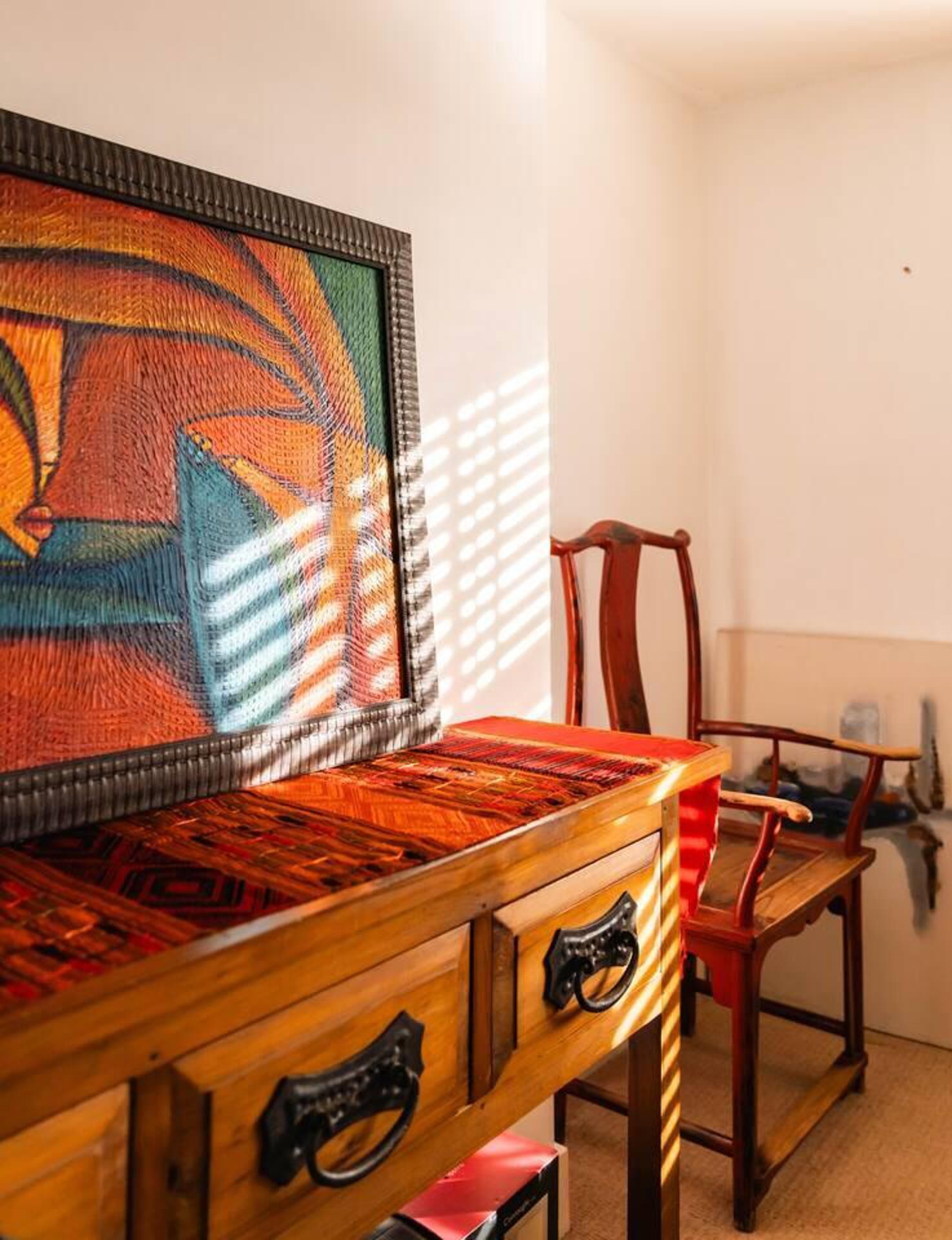 Une table en bois avec des tiroirs, une chaise rouge et un tapis coloré tissé accroché au mur.
