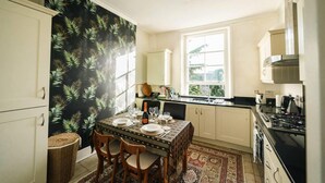A kitchen with a dining table set for four, white cabinets, a large window, and a patterned wall. - Stylish 2 Bedroom Flat in Camden Town (London)