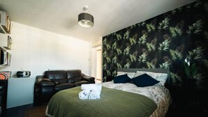 A bedroom with a bed, a chair, a bookshelf, and a wall with a leaf pattern. - Stylish 2 Bedroom Flat in Camden Town (London)