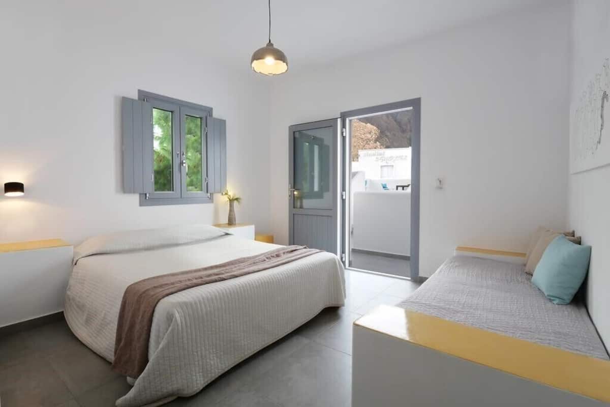A bedroom with a bed, bedside table, lamp, and a view through a door.