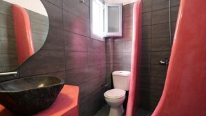 Un baño con un lavabo negro, inodoro blanco y cabina de ducha roja.