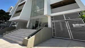 A modern high-rise building with a glass facade, a central entrance with steps, and a metal gate. - Apartamento loft de 1hab vista al mar (Cartagena)