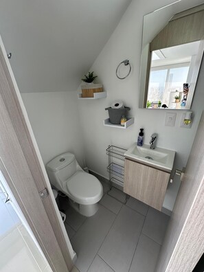 A compact bathroom with a toilet, sink, and storage shelves.