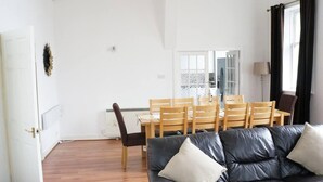 A living room with a black leather sofa, wooden dining table, and chairs. - Rothesay - Apartment - Sleeps9 - Petsok - Parking (Rothesay)