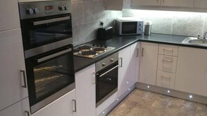 A modern kitchen with stainless steel appliances, white cabinets, and a tiled backsplash. - Rothesay - Apartment - Sleeps9 - Petsok - Parking (Rothesay)