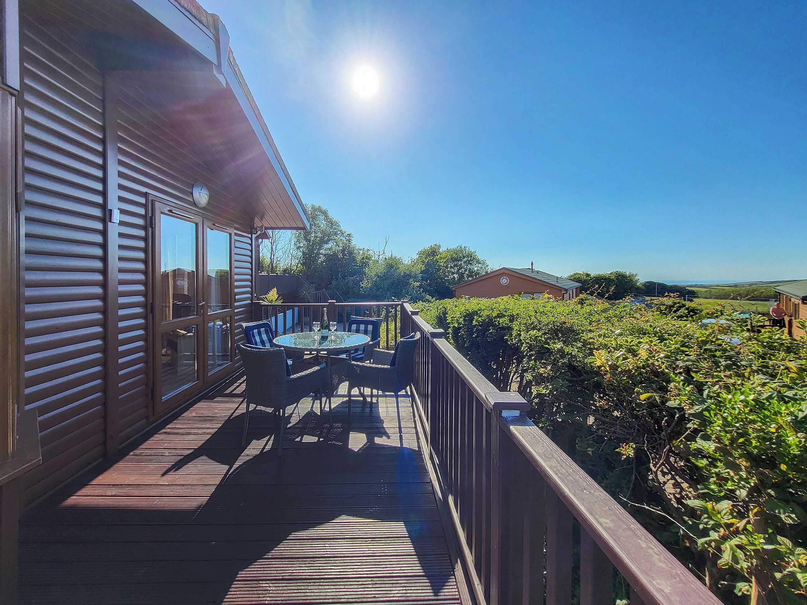 En træterrasse med et glasbord og stole, der giver udsigt over et grønt landskab og et fjerntliggende vue.