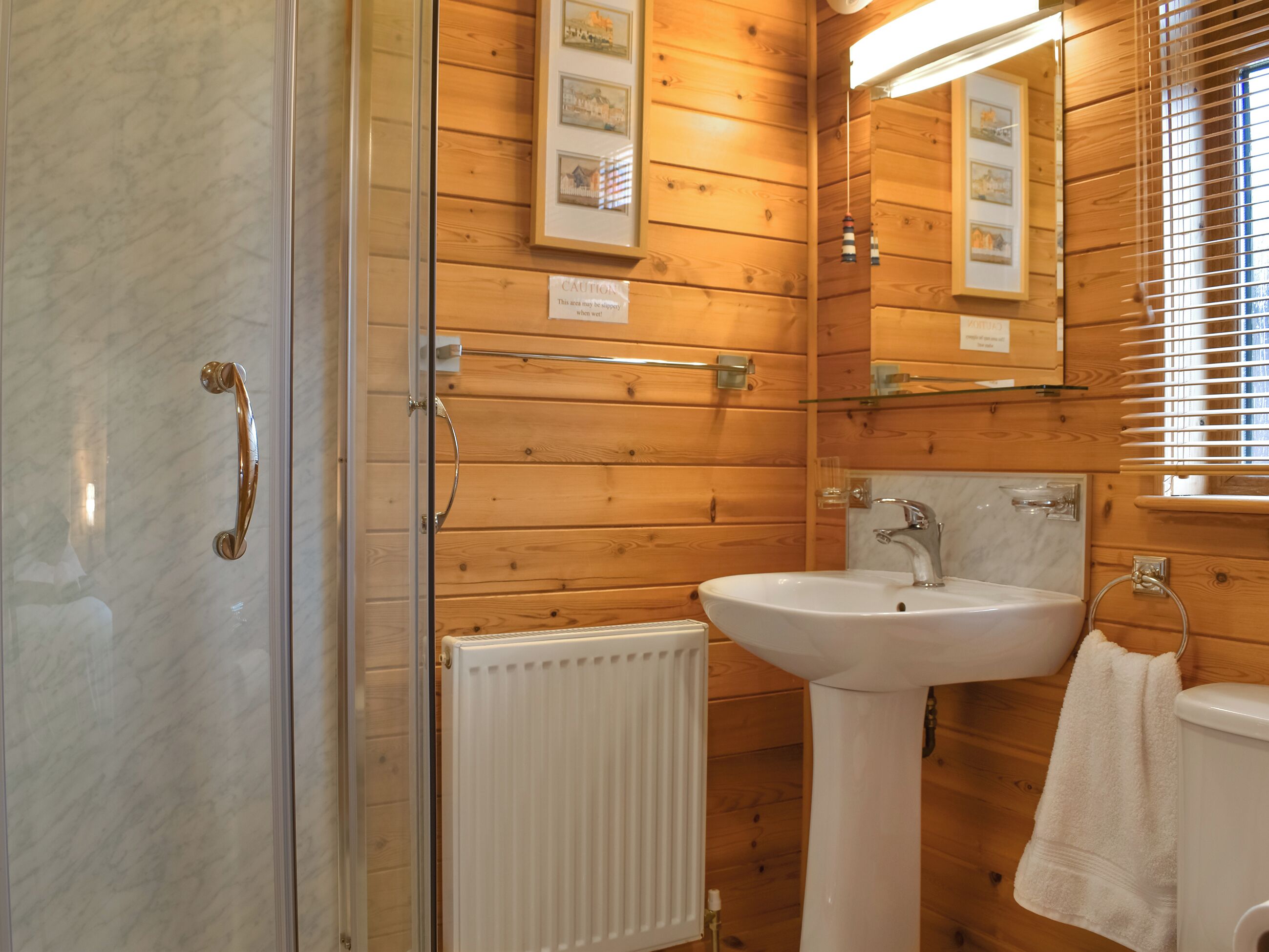 Un intérieur en bois avec une cabine de douche en verre, un lavabo blanc et un porte-serviettes.