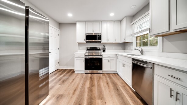 Une cuisine moderne avec des meubles blancs, des appareils en acier inoxydable et un plancher en bois.