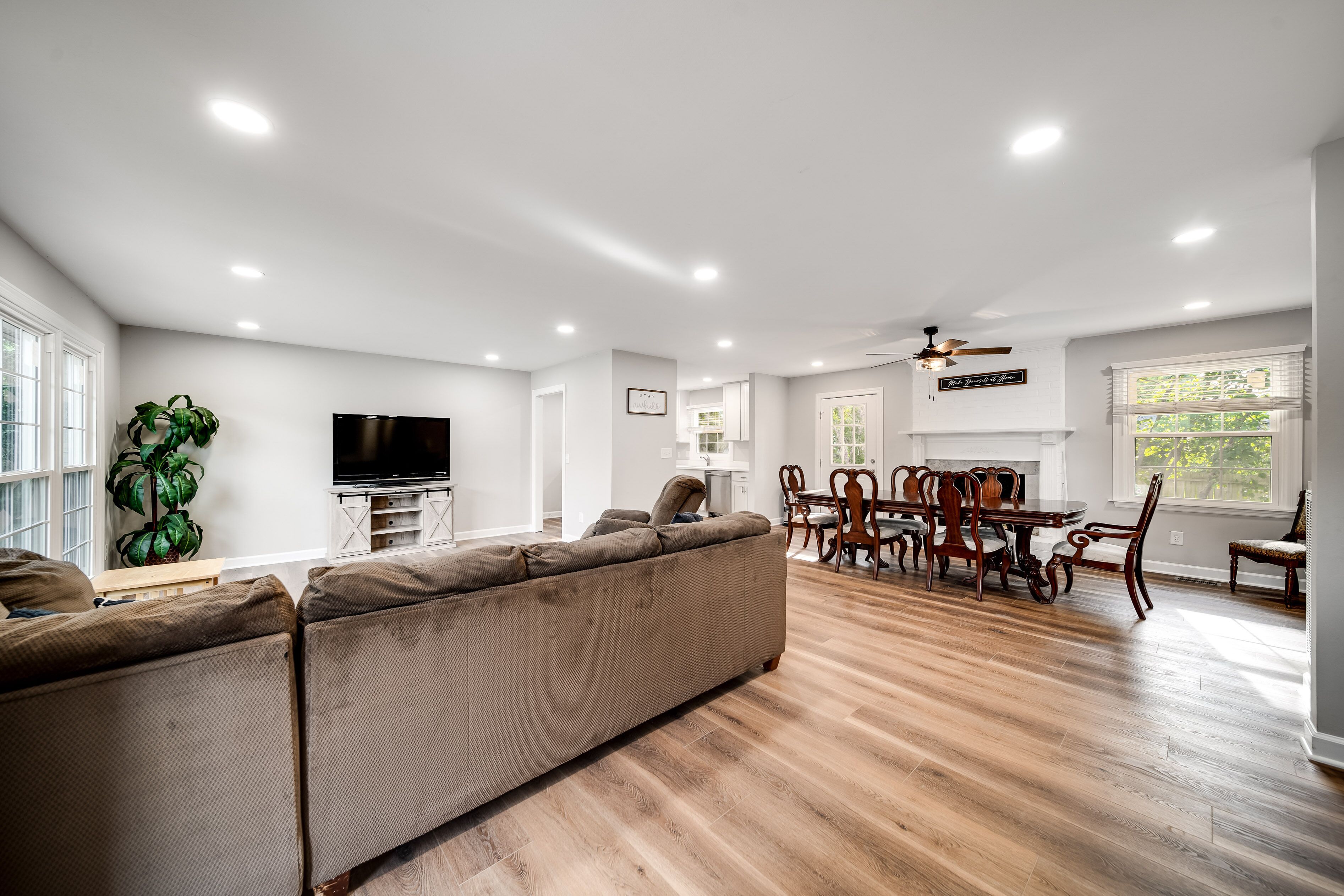 A spacious living room with a large sofa, dining area with wooden furniture, and a flat-screen TV.
