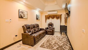 A living room with a leather sofa, a recliner, a patterned rug, and a flat-screen TV mounted on the wall. - Le'Lavion's Pool Villa w/Airport svc. & Private Chef/Ocho Rios Tower Isle (Ocho, Rios, Jamaca)