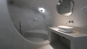 Un baño moderno con una bañera independiente, un espejo redondo y un lavabo blanco.