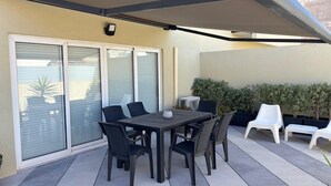 Terrassa exterior amb taula i caires, una tenda retràctil i una porta corredissa de vidre.