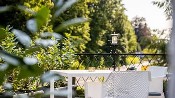 Ein weißes Tisch- und Stuhlsitzset auf einem Balkon mit Metallgeländer, umgeben von Topfpflanzen und einer Laterne.